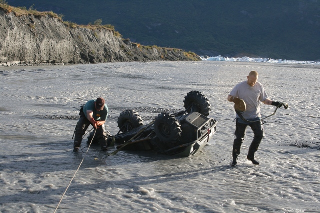 Overturned ATV in water with two people pulling on ropes