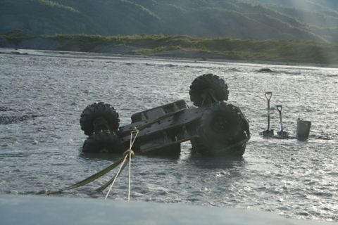 1990 Chevrolet Suburban - An off-road vehicle is stuck in a river, with shovels and a bucket on the bank.
