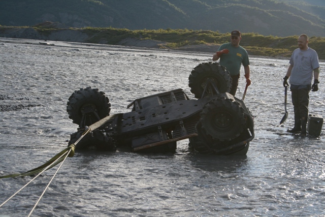 Overturned ATV being recovered from shallow water by two men with shovels