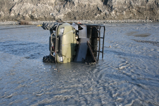 ATV flipped on its side in a shallow, rocky river, being pulled by a cable