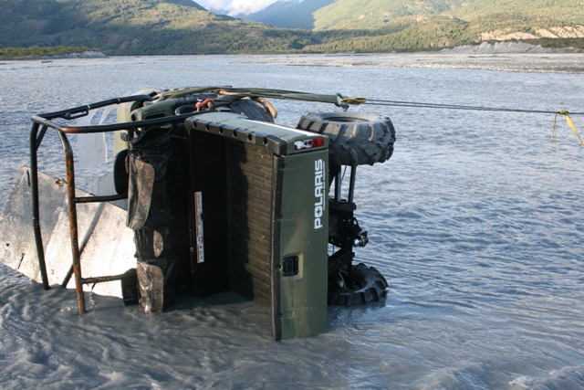 Olive green Polaris ATV on its side in shallow water, being towed