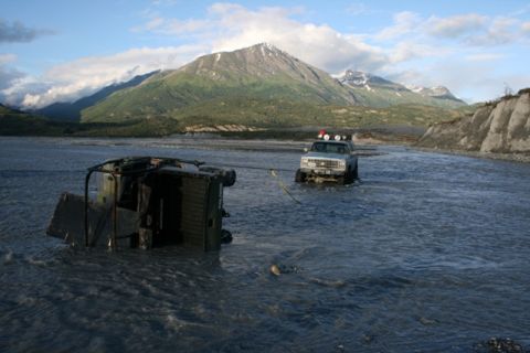 1990 Chevrolet Suburban - Two off-road vehicles are in a river, with one vehicle being towed while overturned.