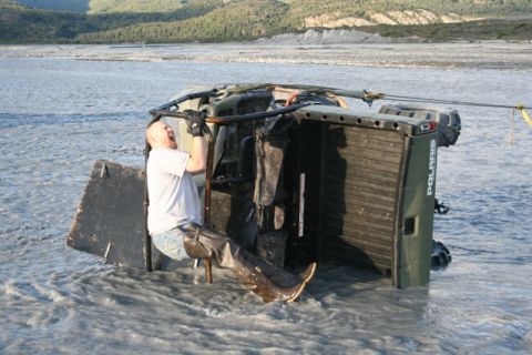 1990 Chevrolet Suburban - An ATV is submerged in a river with a person attempting to recover it.