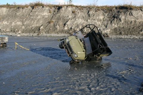 1990 Chevrolet Suburban - A pickup truck tows an ATV out of a shallow river with a steep bank in the background.