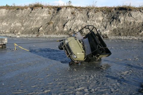 1990 Chevrolet Suburban - A pickup truck tows an ATV out of a riverbed, with a steep embankment in the background.