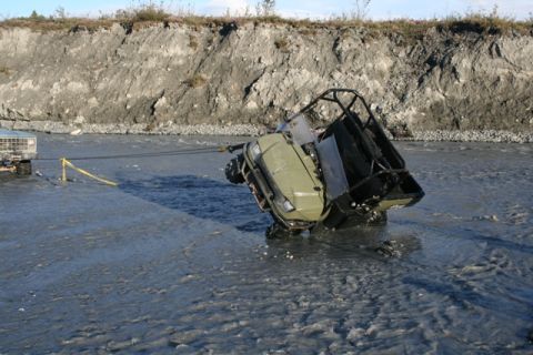 1990 Chevrolet Suburban - A truck is pulling an ATV from a river. The ATV is on its side and partially submerged.