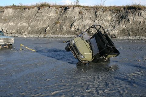 1990 Chevrolet Suburban - A pickup truck tows an ATV out of a riverbed, with a steep embankment in the background.