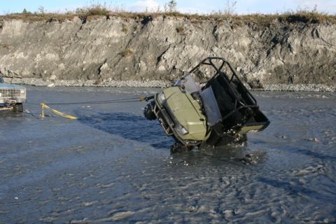 1990 Chevrolet Suburban - A truck is pulling an ATV out of a muddy riverbed, with a steep bank in the background.