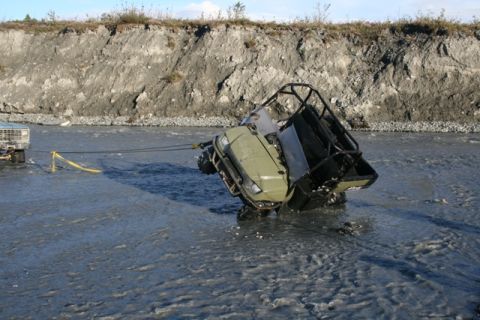 1990 Chevrolet Suburban - A utility vehicle is being towed from a riverbed by a truck.