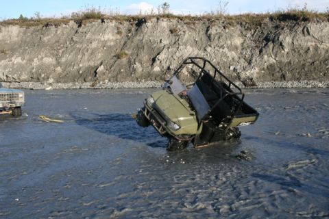 1990 Chevrolet Suburban - Two vehicles are stuck in a muddy riverbed, one is an off-road utility vehicle and the other a pickup truck.