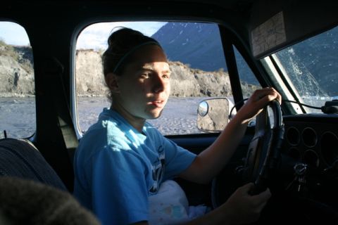1990 Chevrolet Suburban - Driver behind the wheel of a truck, with a scenic view of a river and mountains outside.