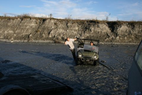 1990 Chevrolet Suburban - A utility vehicle is being pulled from shallow water by another vehicle, with a man leaning on the utility vehicle.