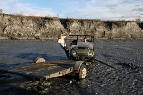 1990 Chevrolet Suburban - Two people in a green utility vehicle tow a trailer through a rocky riverbed.