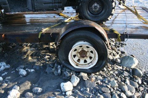 1990 Chevrolet Suburban - A trailer with a flat tire and a portion of a vehicle is situated on a rocky shore next to water.