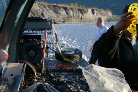 1990 Chevrolet Suburban - A Polaris Ranger ATV is loaded onto a trailer by a rocky riverbank, with two people present.