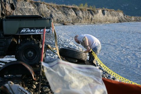 1990 Chevrolet Suburban - A man works on a tire next to a Polaris Ranger ATV by a riverbank.