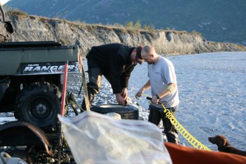 1990 Chevrolet Suburban - Two men work on a tire next to a Polaris Ranger ATV by a river.