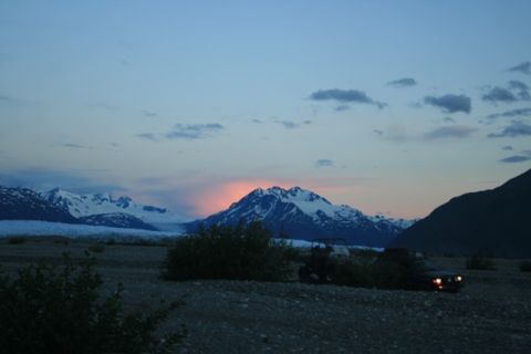 1990 Chevrolet Suburban - Two off-road vehicles are parked in a rocky, desolate landscape with snow-capped mountains in the background during twilight. The vehicle o…