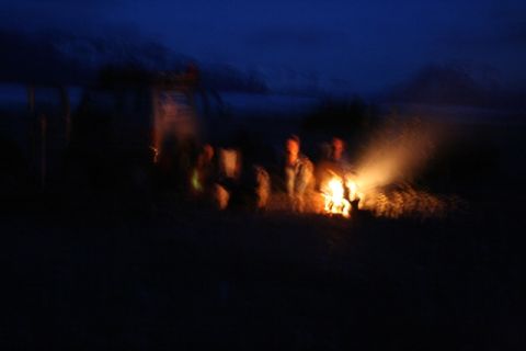 1990 Chevrolet Suburban - A group of people are gathered around a campfire at night. The scene is dark with the fire providing the main source of light.
