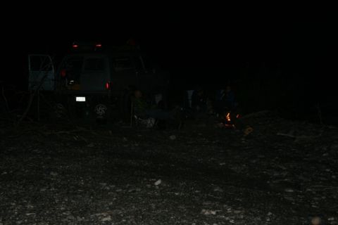 1990 Chevrolet Suburban - A group of people are gathered around a campfire at night next to a van with its rear door open. The van appears to be parked on a gravelly…
