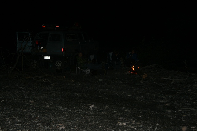 People gathered around a campfire at night next to an open van.