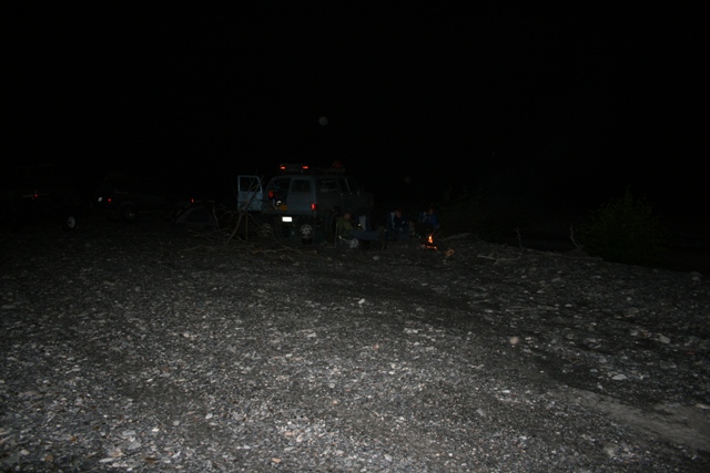 Dark SUV parked at night with people around a campfire.