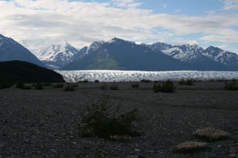 1990 Chevrolet Suburban - A vast glacier stretches across the middle ground, framed by snow-capped mountains under a cloudy sky. The foreground is a rocky, barren pl…