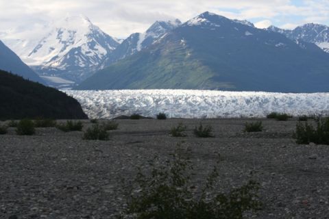 1990 Chevrolet Suburban - A vast glacier stretches across the middle ground, backed by imposing, snow-capped mountains under a cloudy sky. The foreground is a rocky,…