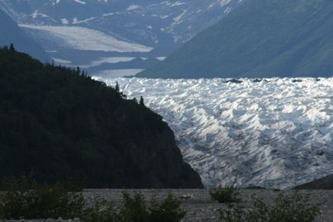 1990 Chevrolet Suburban - A vast glacier stretches across a valley, flanked by dark, forested mountains on the left and lighter, snow-capped mountains in the distanc…