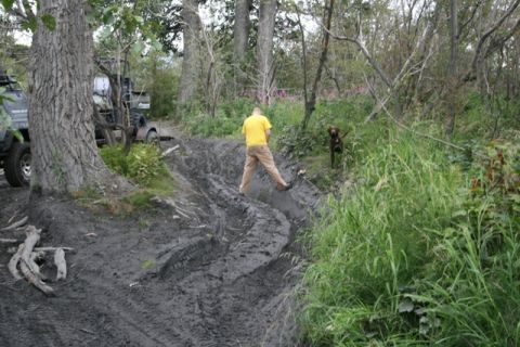 1990 Chevrolet Suburban - A man in a yellow shirt and tan pants stands on a muddy trail next to a brown dog. A portion of a dark-colored SUV is visible on the left s…