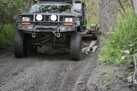 1990 Chevrolet Suburban - A black Jeep Cherokee is shown from the front, pulling a small trailer through a muddy, wooded area. The vehicle has a winch and auxiliary…