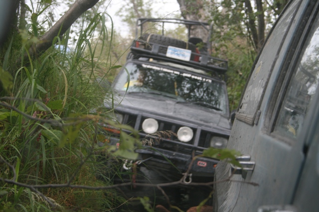 Two off-road SUVs partially hidden by trees and bushes.