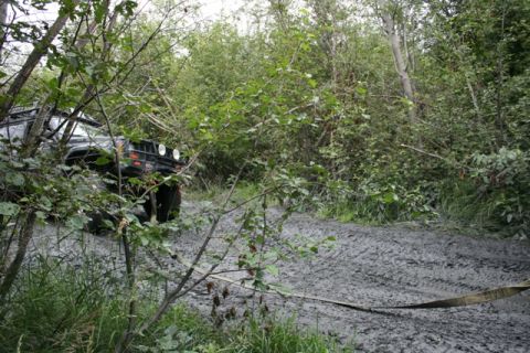 1990 Chevrolet Suburban - A black SUV is stuck in deep mud on a wooded trail, with a tow strap visible on the ground.
