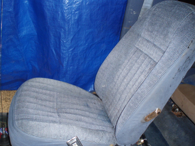 Gray cloth bench seat removed from a vehicle, sitting on a garage floor against a blue tarp