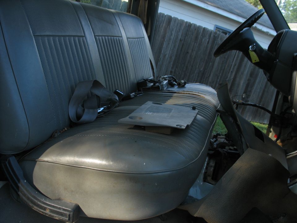 Interior of a vehicle showing a gray bench seat and steering wheel.