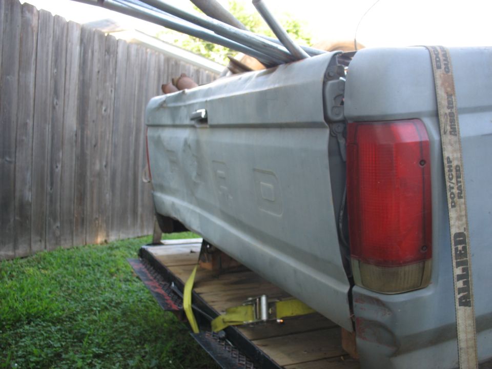 Light gray pickup truck bed on a trailer, showing damage and a red taillight.