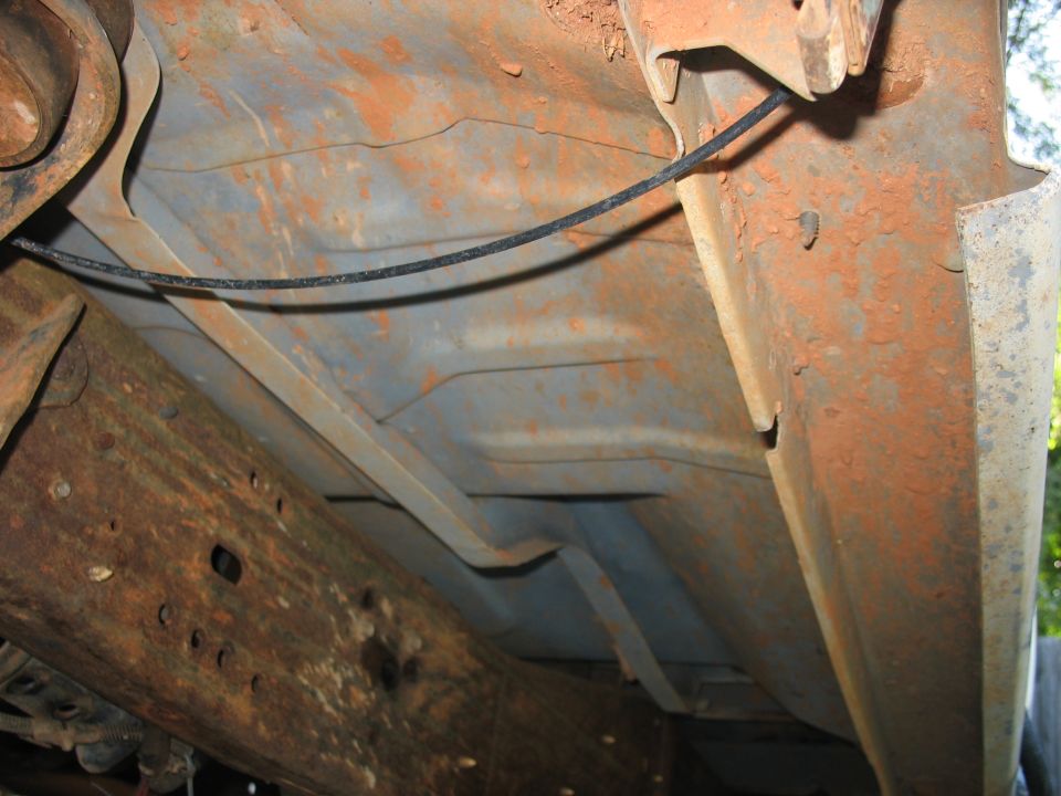 Underside of a rusty vehicle frame with a black cable.