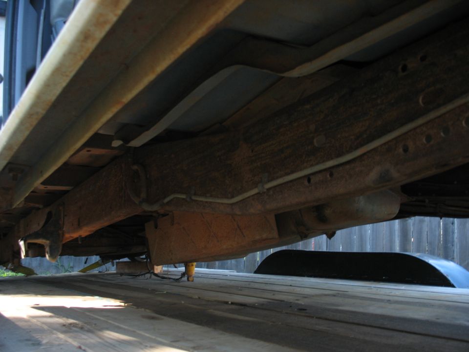 Underside of a vehicle, showing rusty frame and suspension components. A white object is visible below