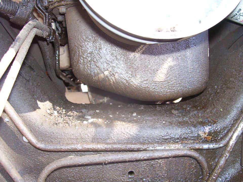 Underside of a vehicle with oil leaks, showing fuel lines and engine components.