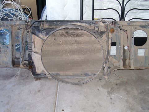 1991 Ford Bronco - A dirty radiator and fan shroud assembly is shown from the front, likely removed from a 1991 Ford Bronco. The assembly is resting on a conc…