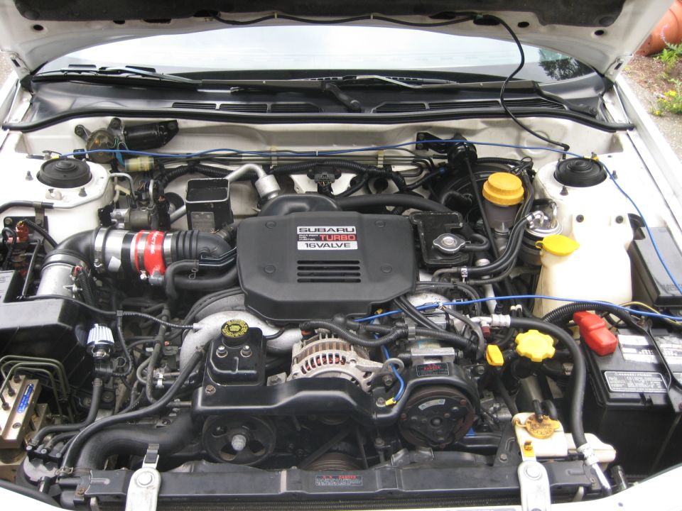 Subaru turbocharged engine bay with black engine cover, red intercooler hose, and various hoses and wires.