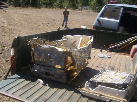 1986 Ford Bronco - The bed of a pickup truck is filled with damaged metal debris and what appears to be a broken appliance. A person stands in the background…