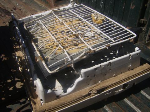 1986 Ford Bronco - A white, heavily rusted and damaged portable grill sits in the bed of a dark green pickup truck. The grill has a white wire rack on top and…