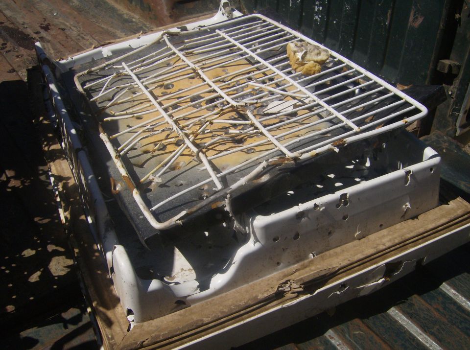 Damaged white portable grill in the bed of a pickup truck.