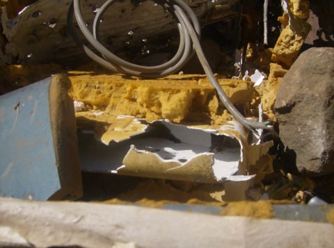 1986 Ford Bronco - A close-up view of damaged yellow foam insulation and a gray cable, with a large rock visible on the right. The scene appears to be outdoor…