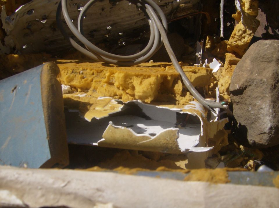 Damaged yellow foam insulation and a gray cable with a rock.