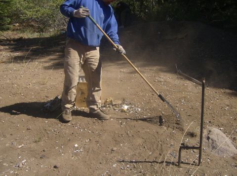 1986 Ford Bronco - A person wearing a blue sweatshirt and tan pants is raking the ground, clearing debris. The scene appears to be outdoors in a wooded or bru…