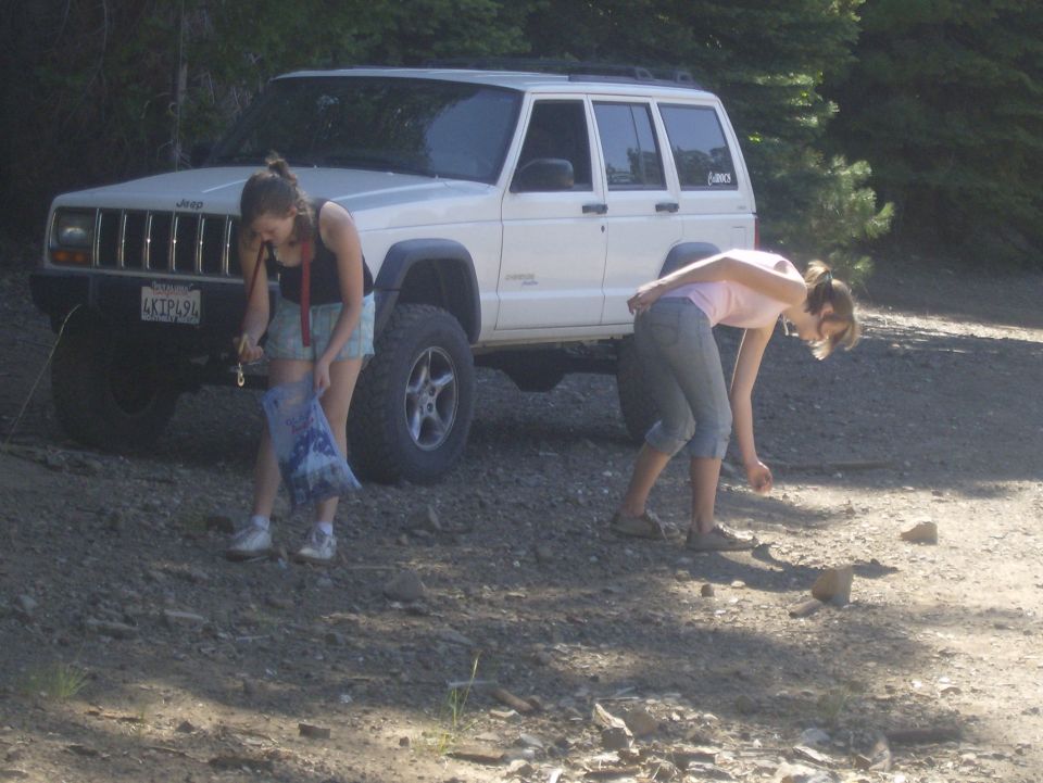 Two women near a white Jeep Cherokee SUV on a dirt road.