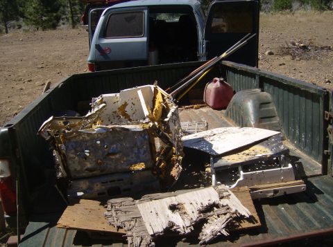 1986 Ford Bronco - The bed of a dark green pickup truck is filled with damaged vehicle parts, including a mangled white and yellow interior component and a re…