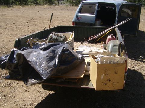 1986 Ford Bronco - The bed of a pickup truck is filled with various items including a large black trash bag, a cardboard box with what appears to be targets,…